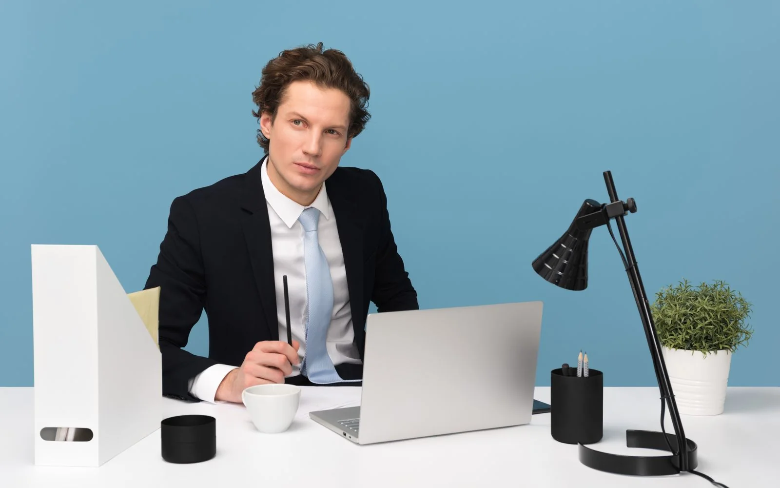 A man working on a laptop at a desk with a lamp
