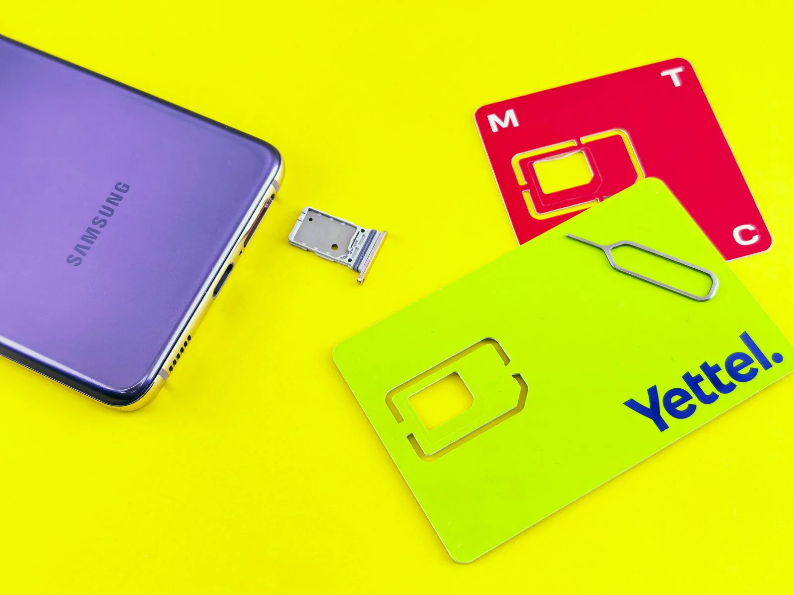 Smartphone with its SIM tray and ejector tool on a yellow background