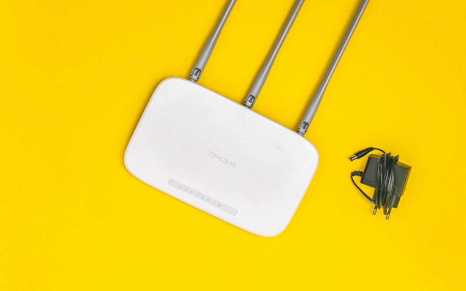 A white Wi-Fi router with three antennas on a yellow background